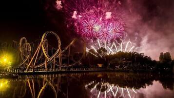 Ein Nachtblick auf einen Park mit Riesenrad und einem Feuerwerk über dem Wasser.