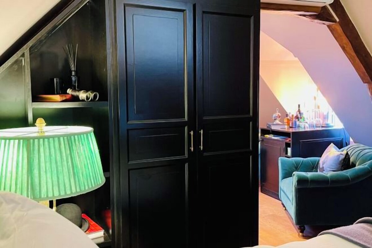Una habitación con un armario oscuro, una lámpara verde, un sofá color esmeralda y una pequeña mesa con objetos encima.