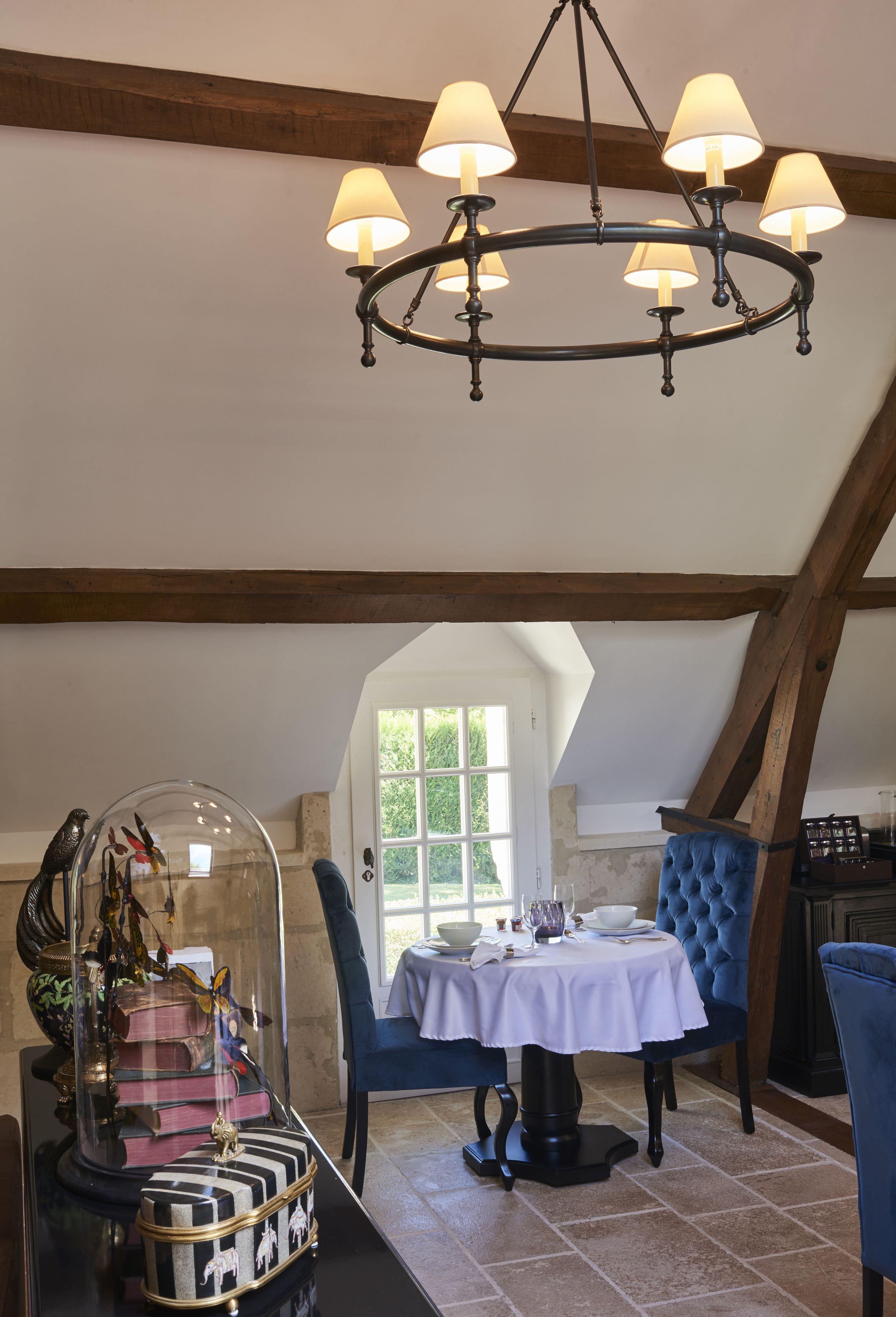 Comedor con candelabro, una mesa dispuesta para dos personas y vistas al exterior a través de una ventana.