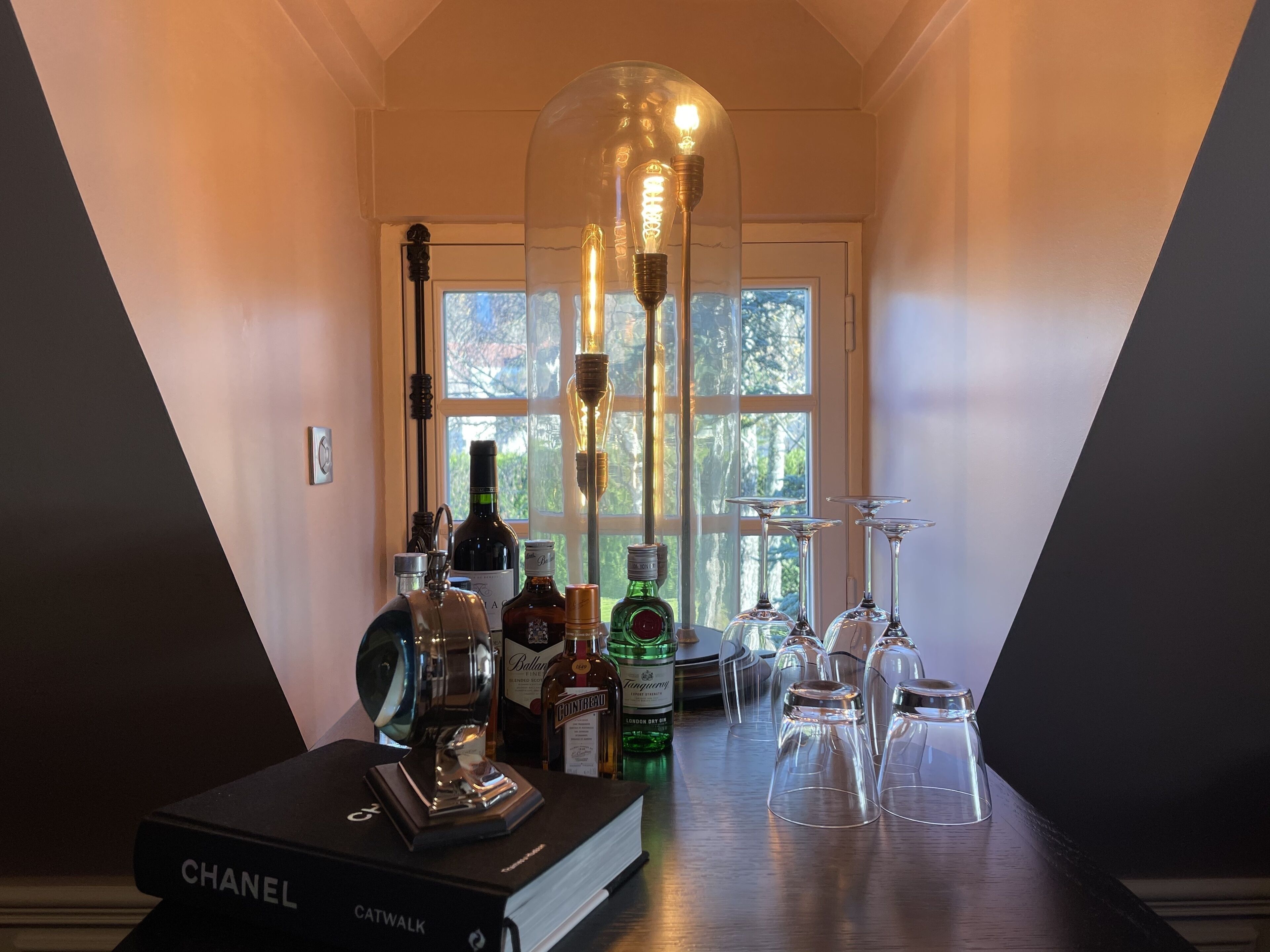 A hallway with a chandelier, wine bottles, glasses, and a Chanel book.