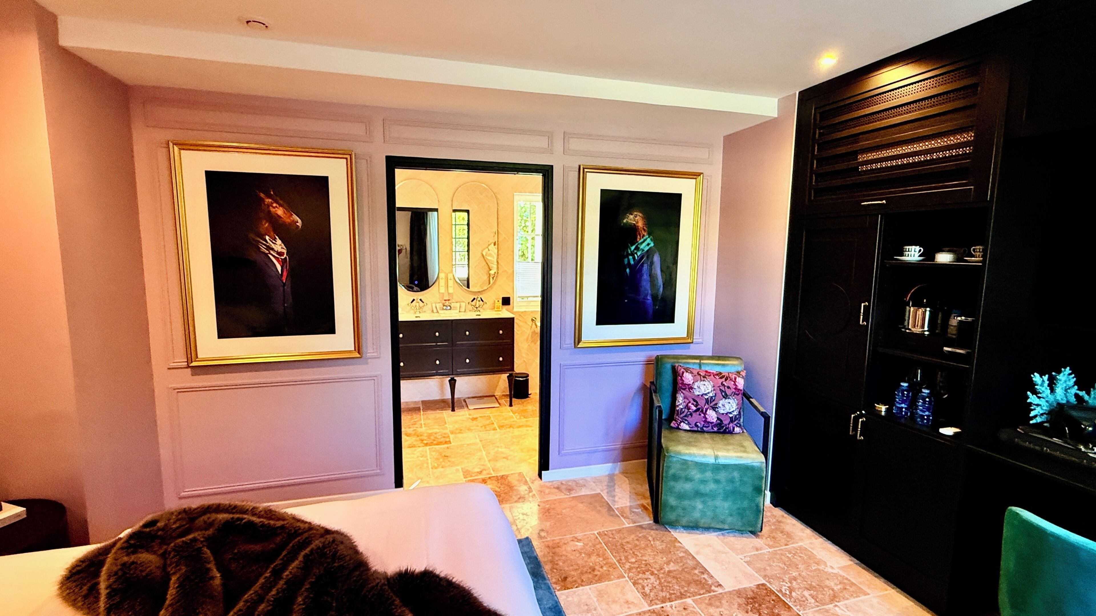 Habitación de hotel con cama, un pequeño rincón de descanso, tocador con espejo y dos cuadros en la pared.