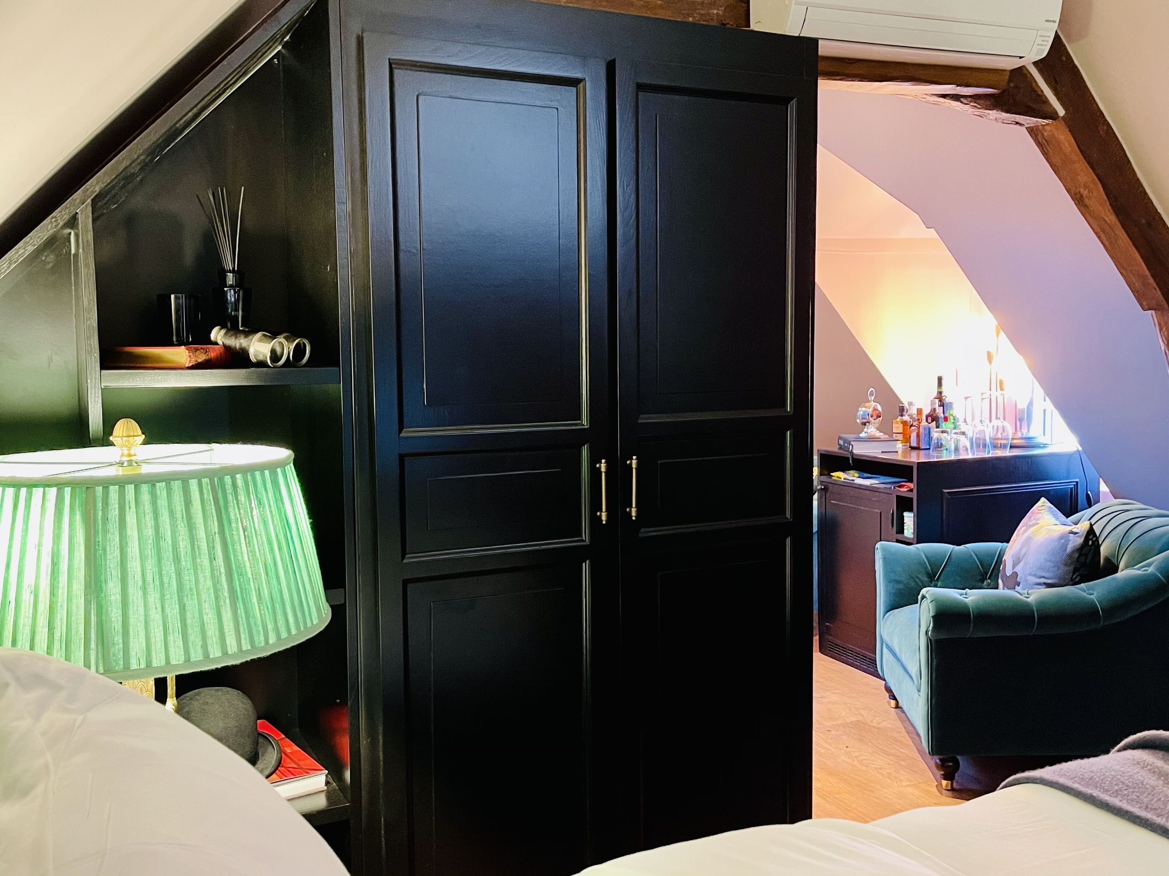 Una habitación con un armario negro, una lámpara verde, un sofá color turquesa y suelo de madera.