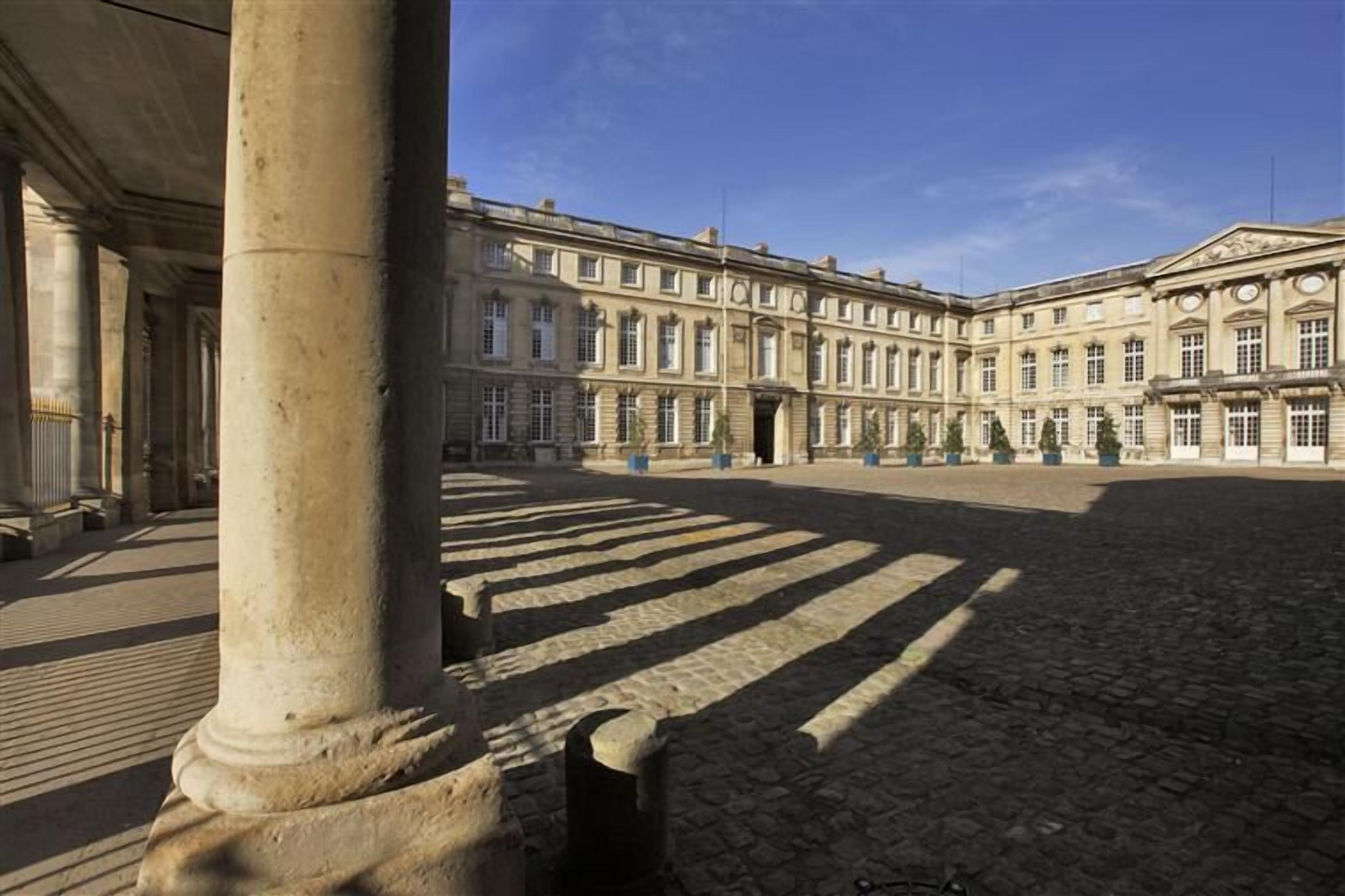 A courtyard with a classical building featuring columns and a symmetrical facade.