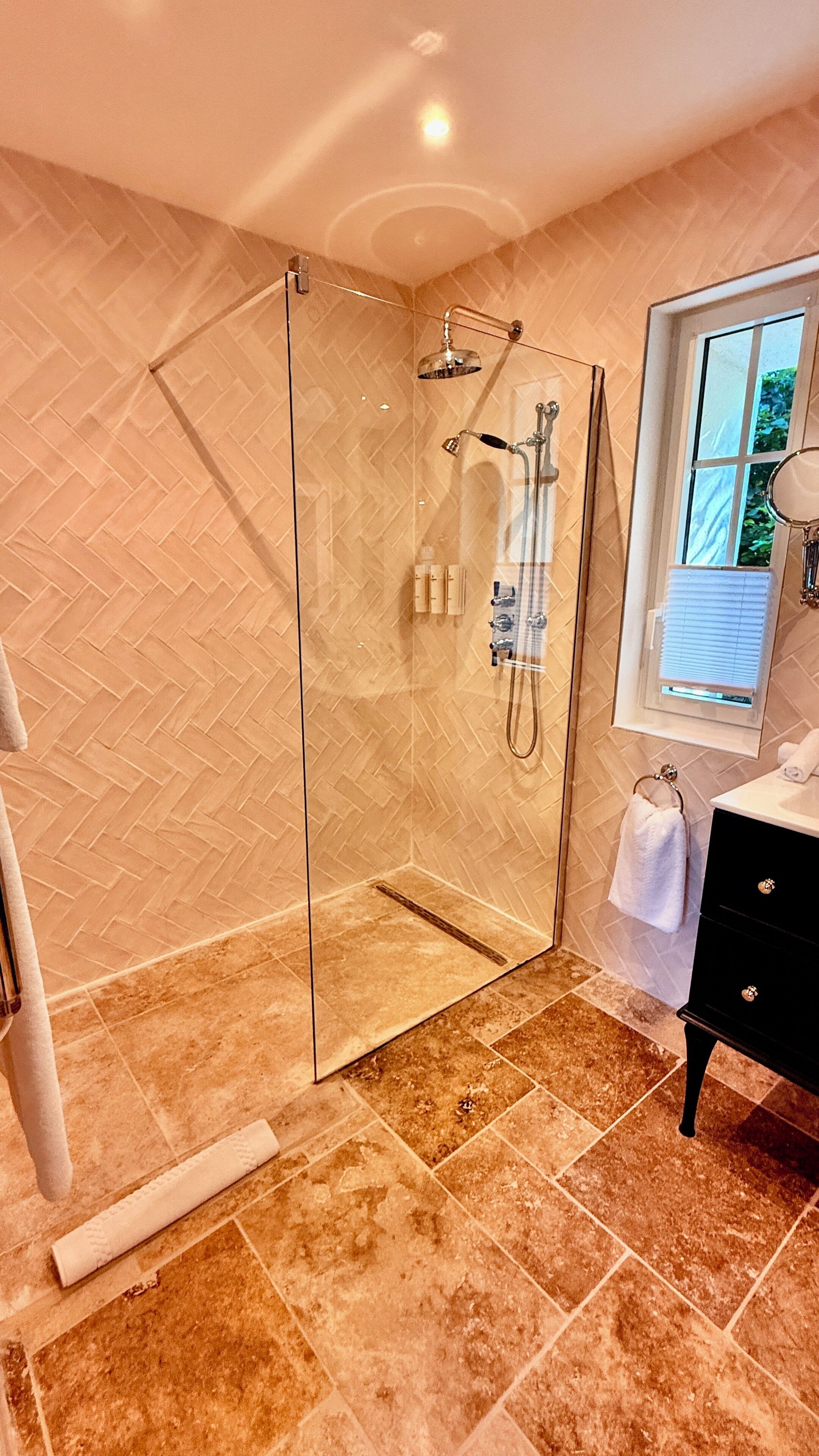A modern bathroom with a glass shower enclosure, a vanity with a mirror, and a window providing natural light.