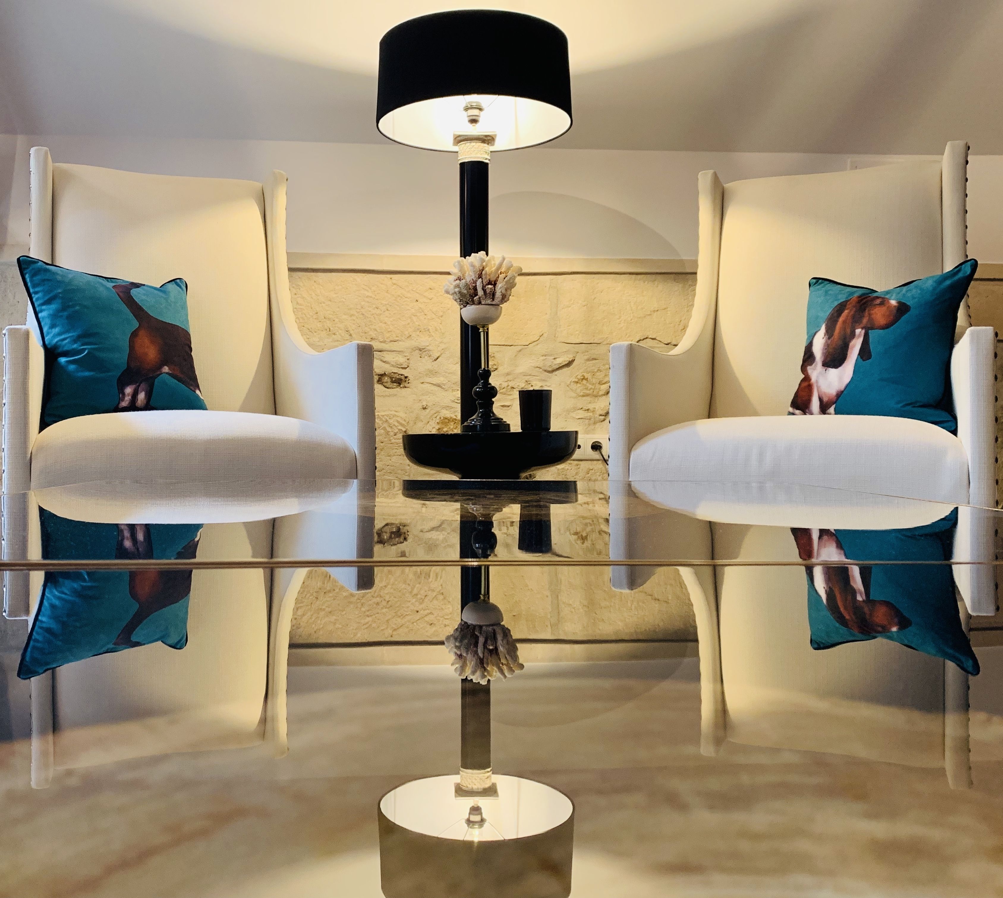 A modern room with a glass table reflecting two white armchairs and a black lamp.