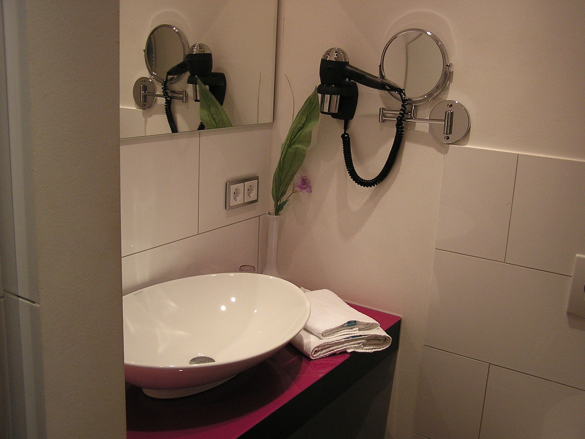 A bathroom with a white sink, a mirror, and a hairdryer mounted on the wall.