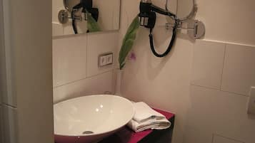 A bathroom with a white sink, a mirror, and a hairdryer mounted on the wall.