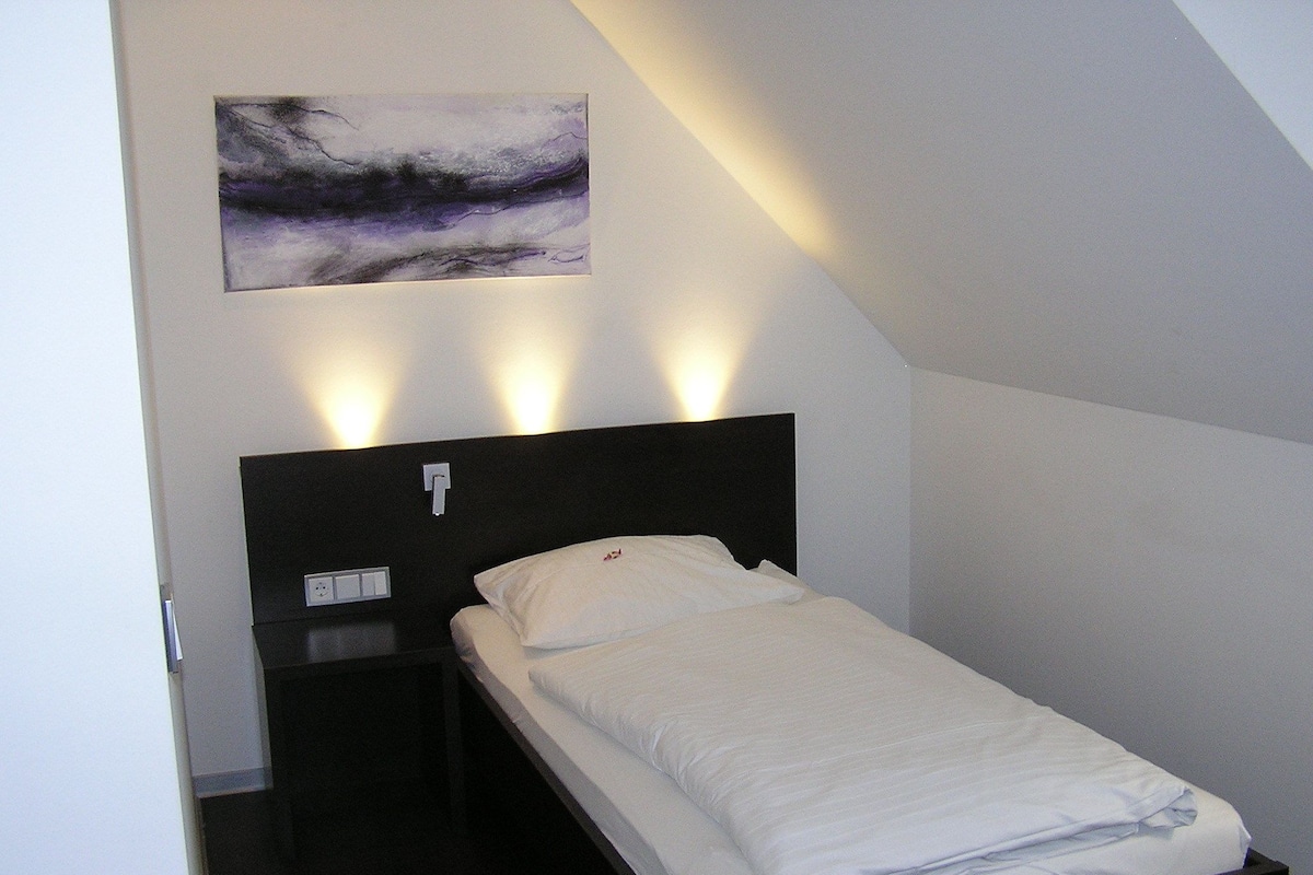A single bed with a black headboard, white bedding, and a wall-mounted light fixture.