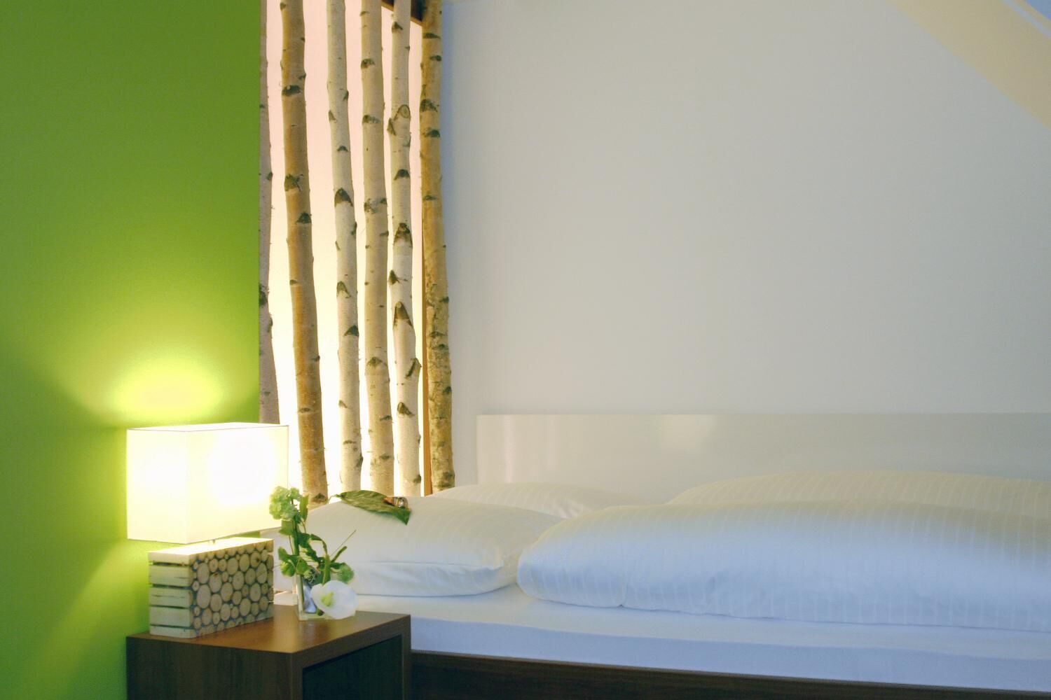 A neatly made bed with white linens, a bedside table with a lamp, and a green wall.