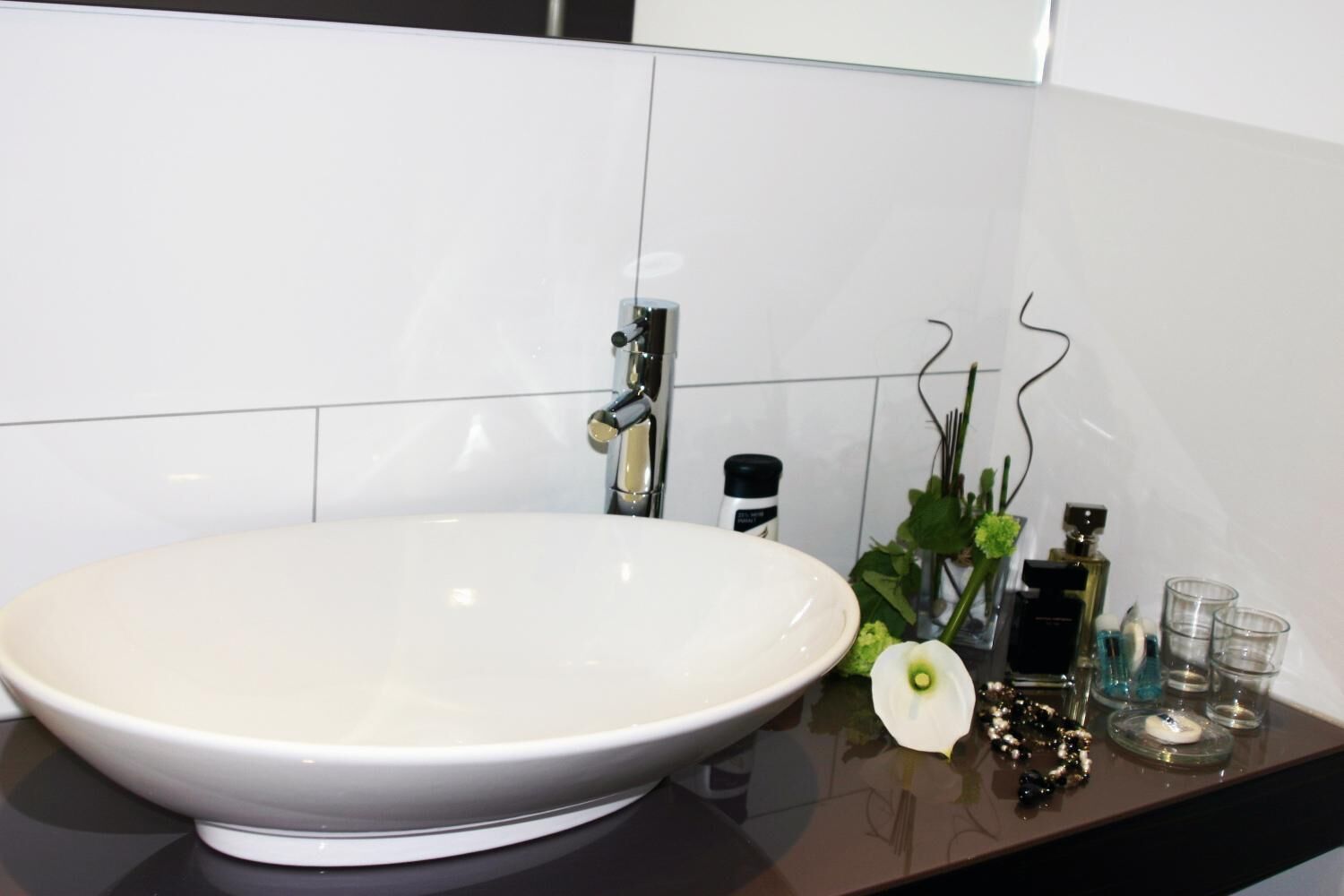 A modern bathroom with a large oval sink, a chrome faucet, and a glass countertop.