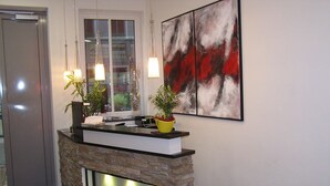 A reception desk with a stone facade, two potted plants, and a modern abstract painting on the wall. - Hotel zur Promenade (Donauwoerth)