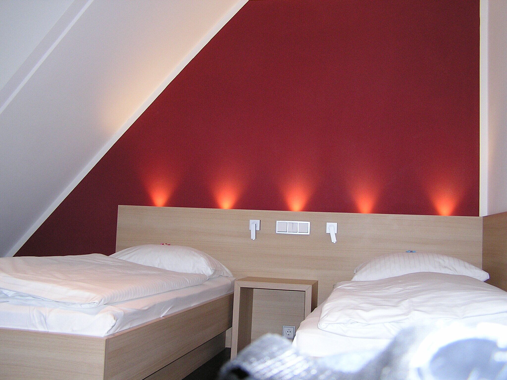 A hotel room with two beds, a wooden headboard, and a red accent wall.