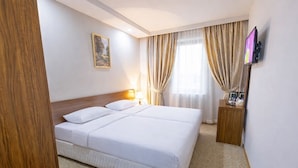 Une chambre d’hôtel avec un grand lit, une table de chevet avec une lampe, un téléviseur fixé au mur et une fenêtre avec des rideaux.