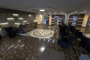 Un vestíbulo con mostrador de recepción, zona de estar y alfombra estampada.