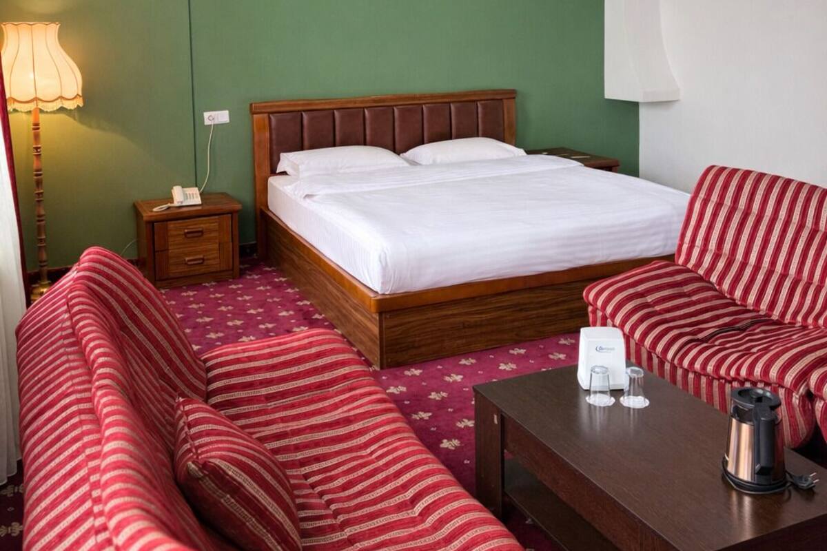 A hotel room with a bed, a sofa, a coffee table, and a lamp.