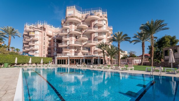 A hotel with a large swimming pool, multiple balconies, and palm trees. - Renovated White 3BD next to Beach - Pool (Eilat)