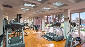 A spacious gym with treadmills, elliptical machines, and weightlifting equipment. Large windows offer views of a swimming pool and outdoor area. - Renovated White 3BD next to Beach - Pool (Eilat)