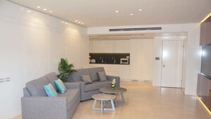 A modern living room with a grey sofa, a small round table, and a potted plant. - Renovated White 3BD next to Beach - Pool (Eilat)
