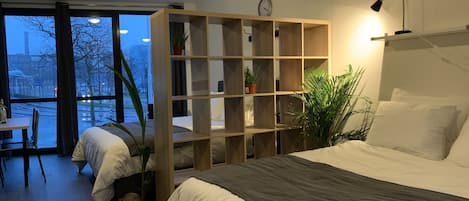 Un dormitorio moderno con una cama grande, una estantería de madera y vista a la calle.