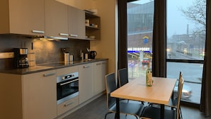 Una cocina moderna con electrodomésticos integrados, un comedor con mesa y sillas, y vistas a un aparcamiento a través de amplias ventanas.