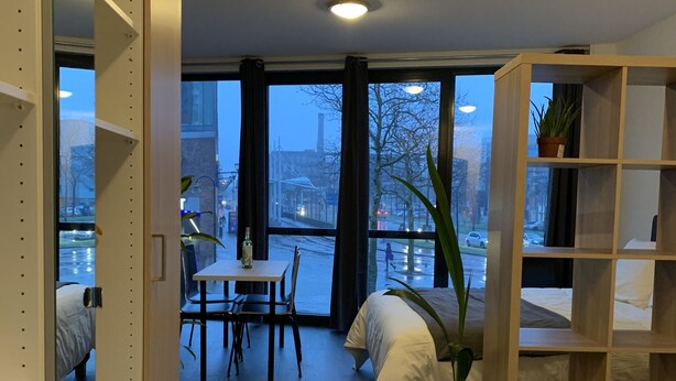 Una habitación de hotel moderna con un ventanal grande, una zona de comedor y una estantería.