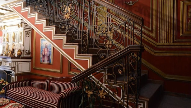 A staircase with ornate metal railings and a red and white striped sofa at the bottom.