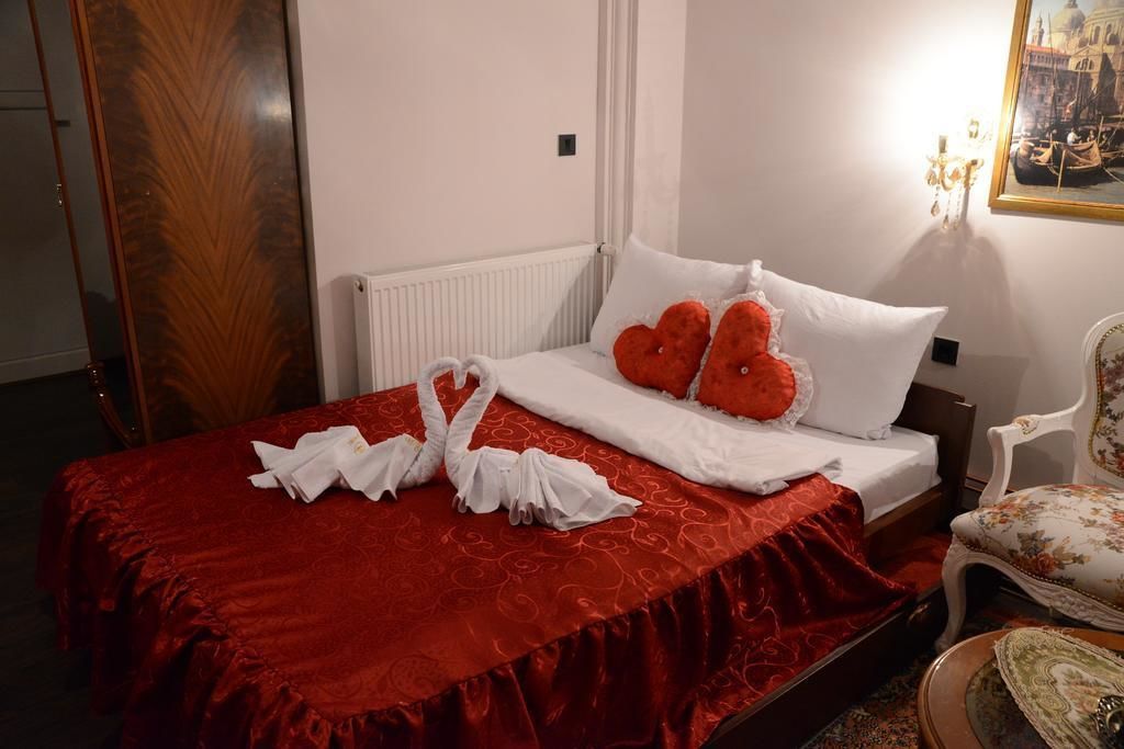 Una cama bien hecha con una colcha roja, dos almohadas con forma de corazón y un par de toallas blancas dispuestas sobre la cama.