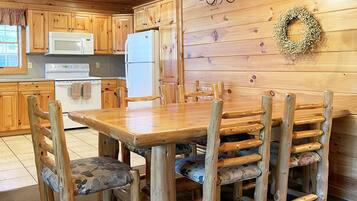 A wooden interior with a dining table and chairs, a refrigerator, and a microwave.