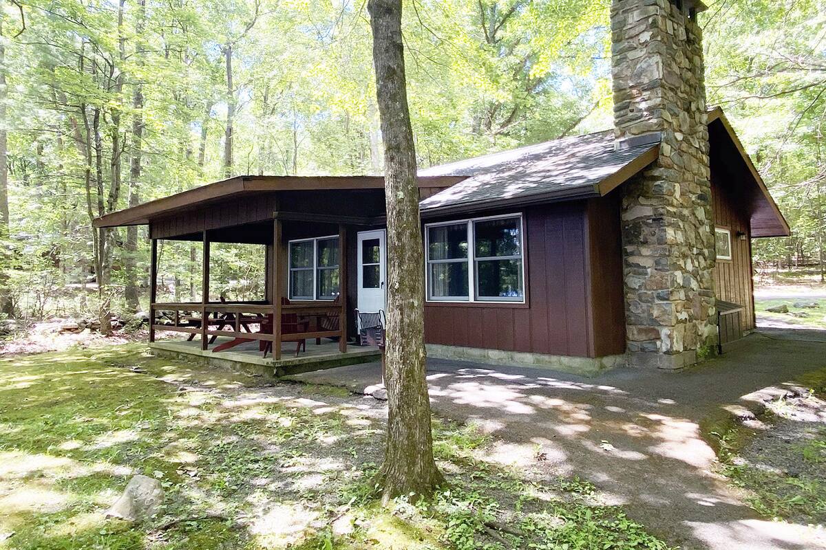A rustic cabin with a stone chimney, a covered porch, and a picnic table.