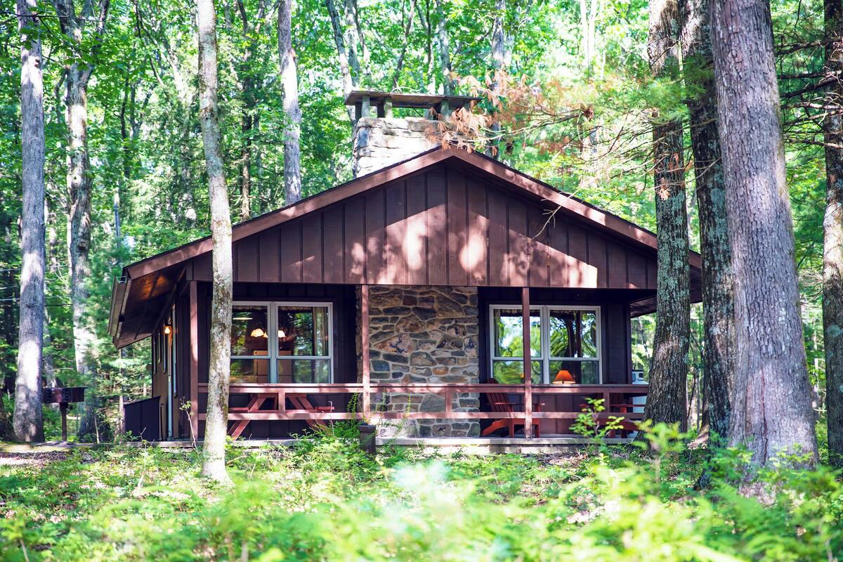 A cabin with a stone foundation, wooden exterior, and a porch with benches.