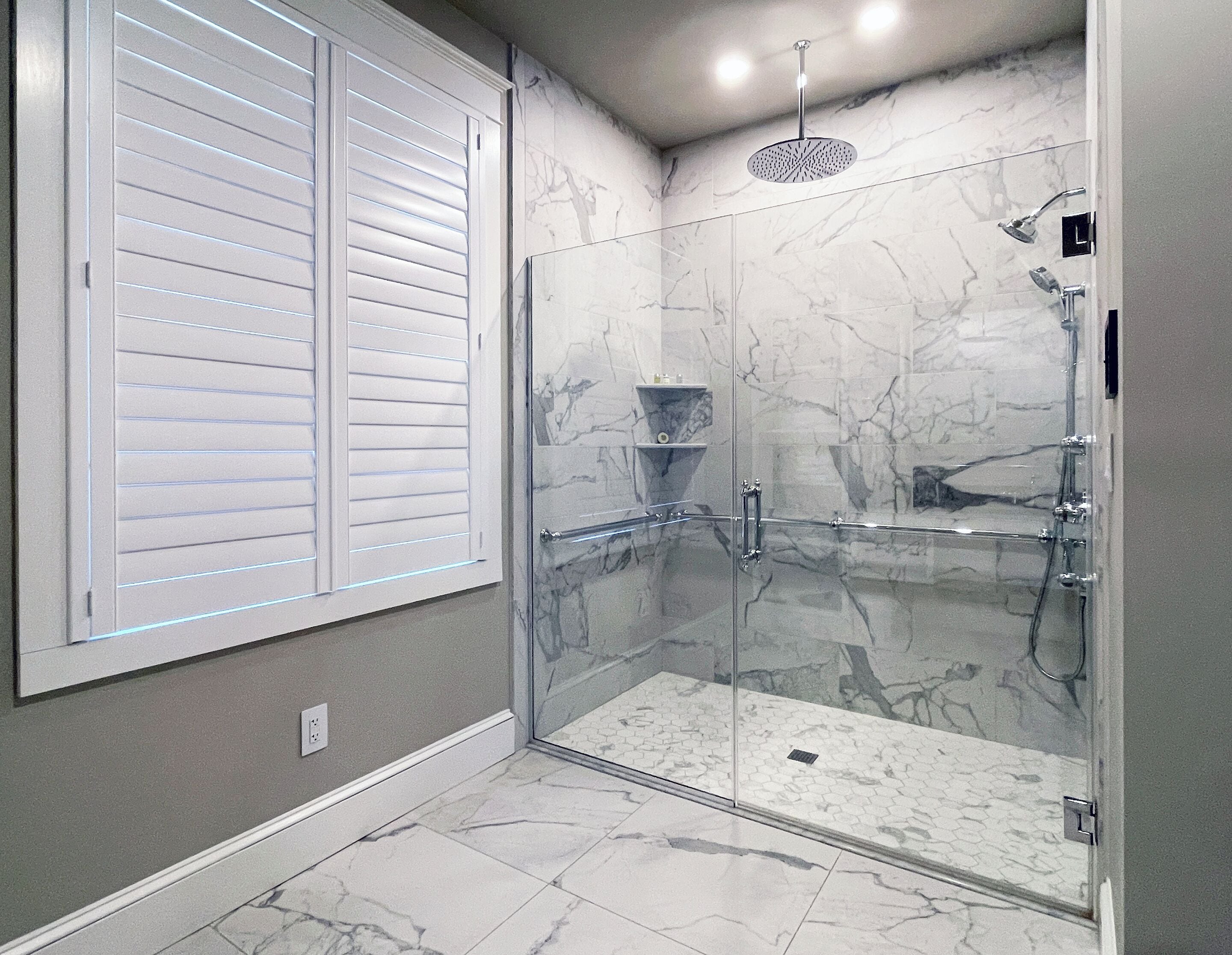 A glass-enclosed walk-in shower with a marble floor and a showerhead.