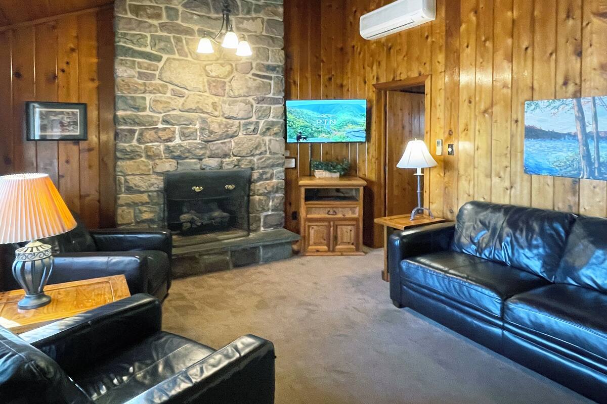 A cozy living room with a stone fireplace, leather sofa, and a television mounted on the wall.