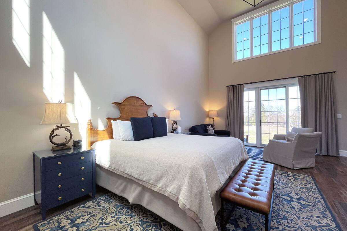 A spacious bedroom with a large bed, a bench, a chair, and a nightstand with lamps.