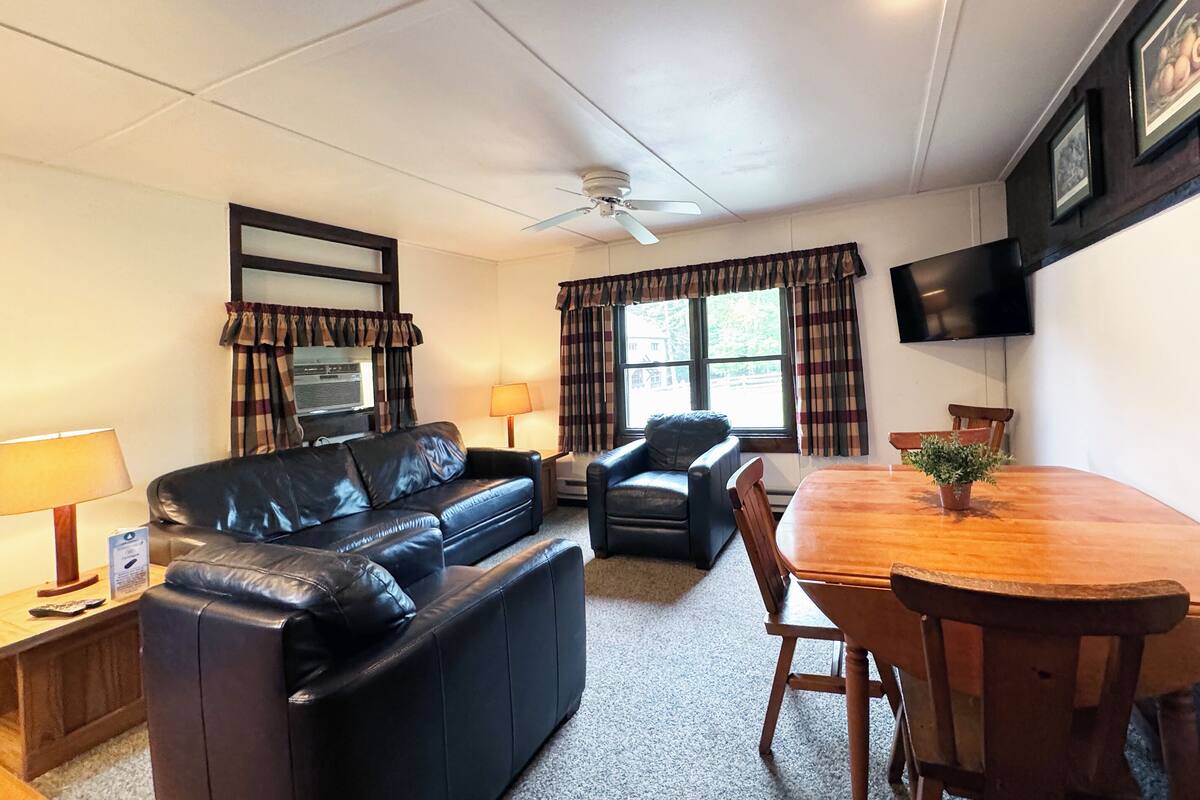 A living room with a black leather sofa, a wooden dining table, and a ceiling fan.