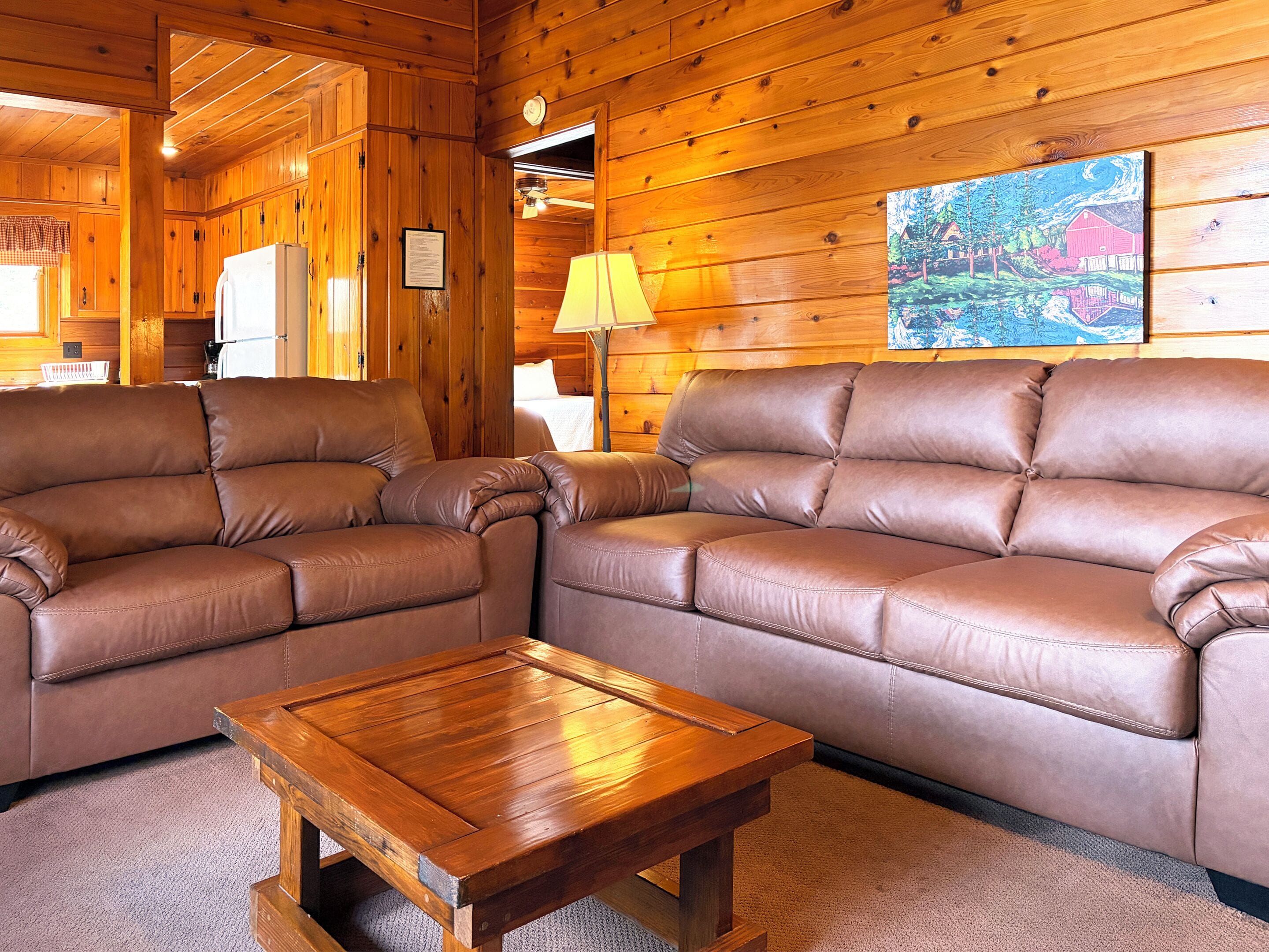 A wooden interior with two leather sofas, a wooden coffee table, and a painting on the wall.