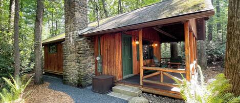 A rustic cabin with a stone chimney, wooden exterior, and a covered porch with seating.