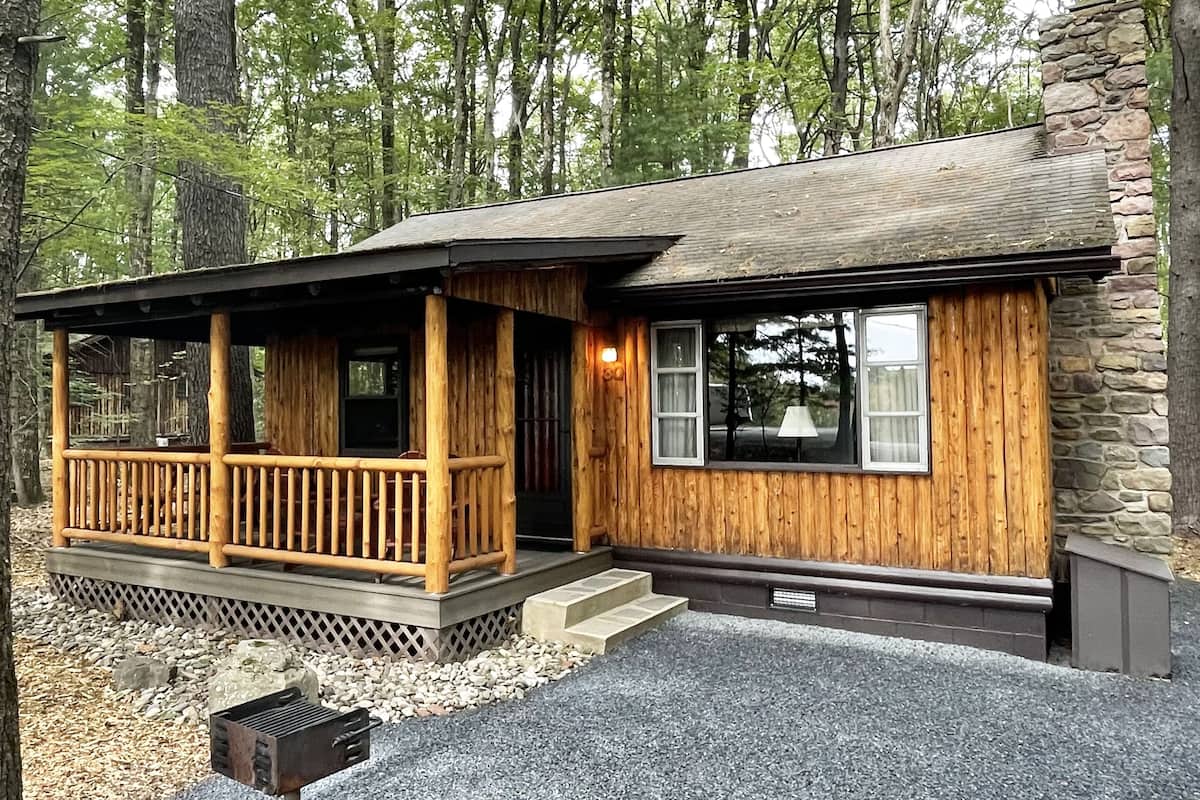 A wooden cabin with a porch, stone exterior, and a gravel driveway.
