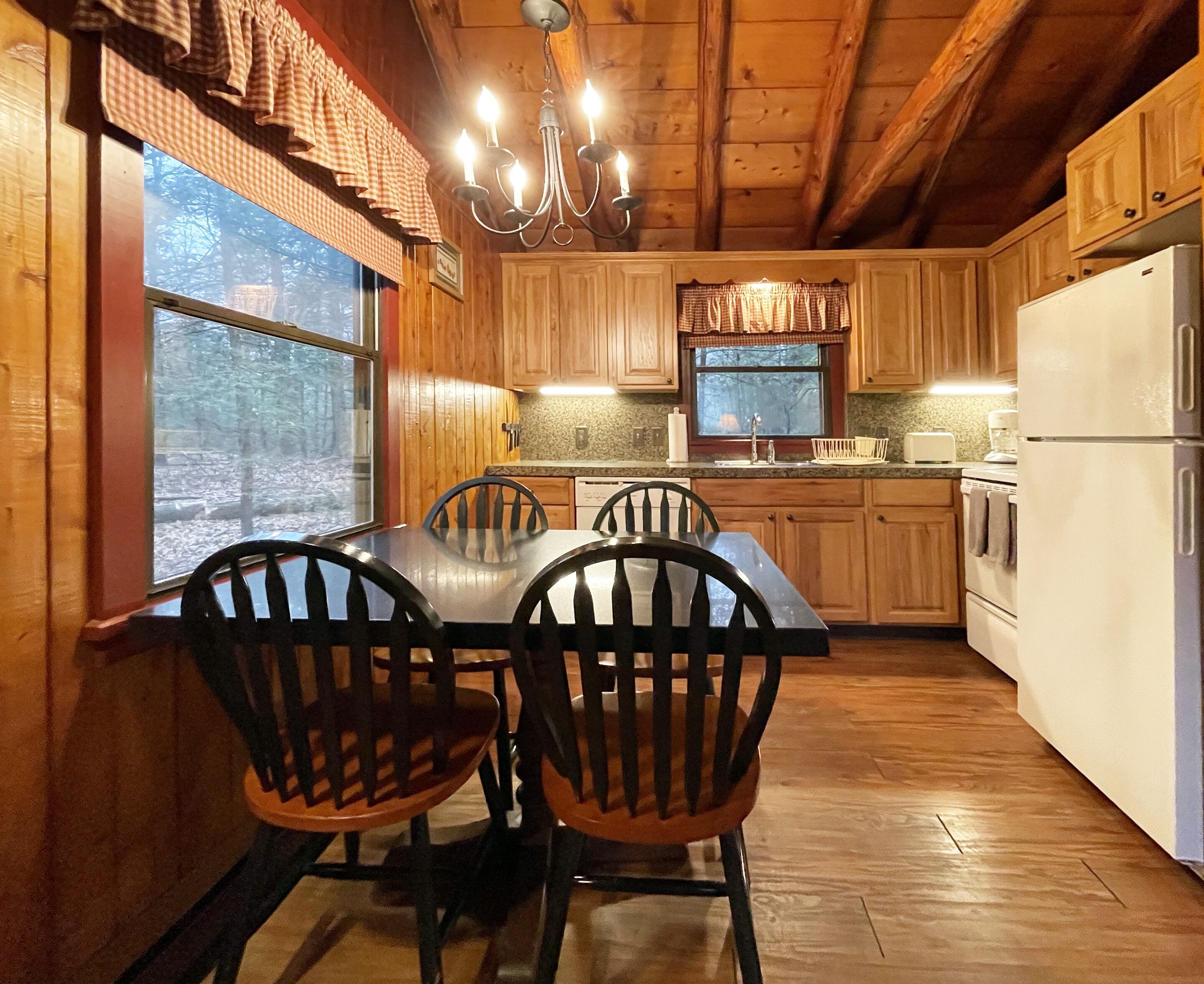 A wooden cabin kitchen with a dining table and chairs, a chandelier, and a refrigerator.