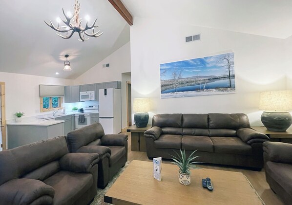 A living room with a brown leather sofa, a coffee table with a remote control, and a painting of a winter landscape on the wall.