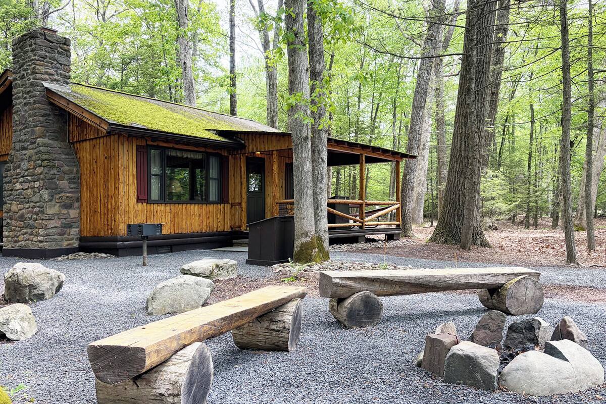 A rustic cabin with a stone chimney, wooden walls, and a covered porch.