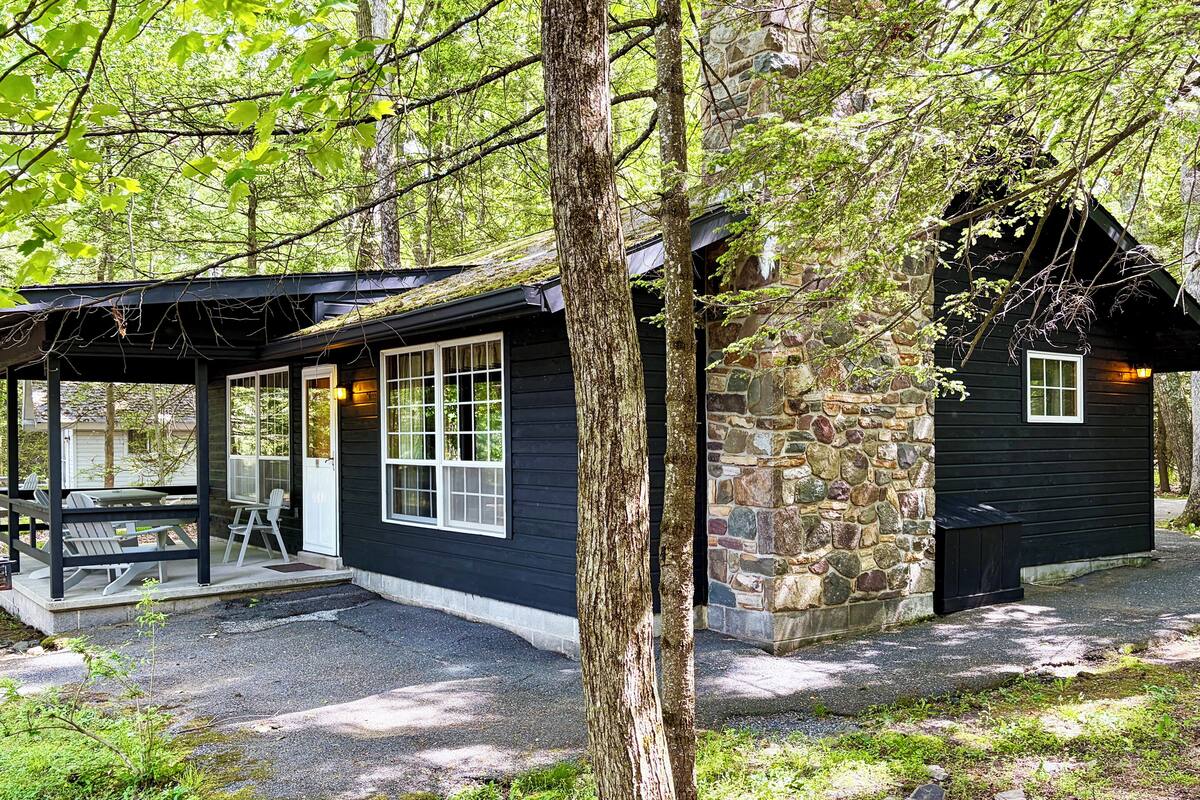 A cabin with a porch, stone wall, and a small attached structure.