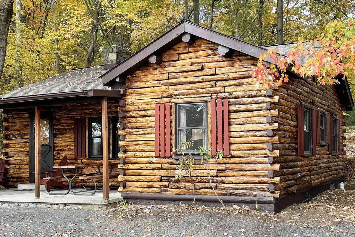 A log cabin with a porch, picnic table, and red Adirondack chairs.