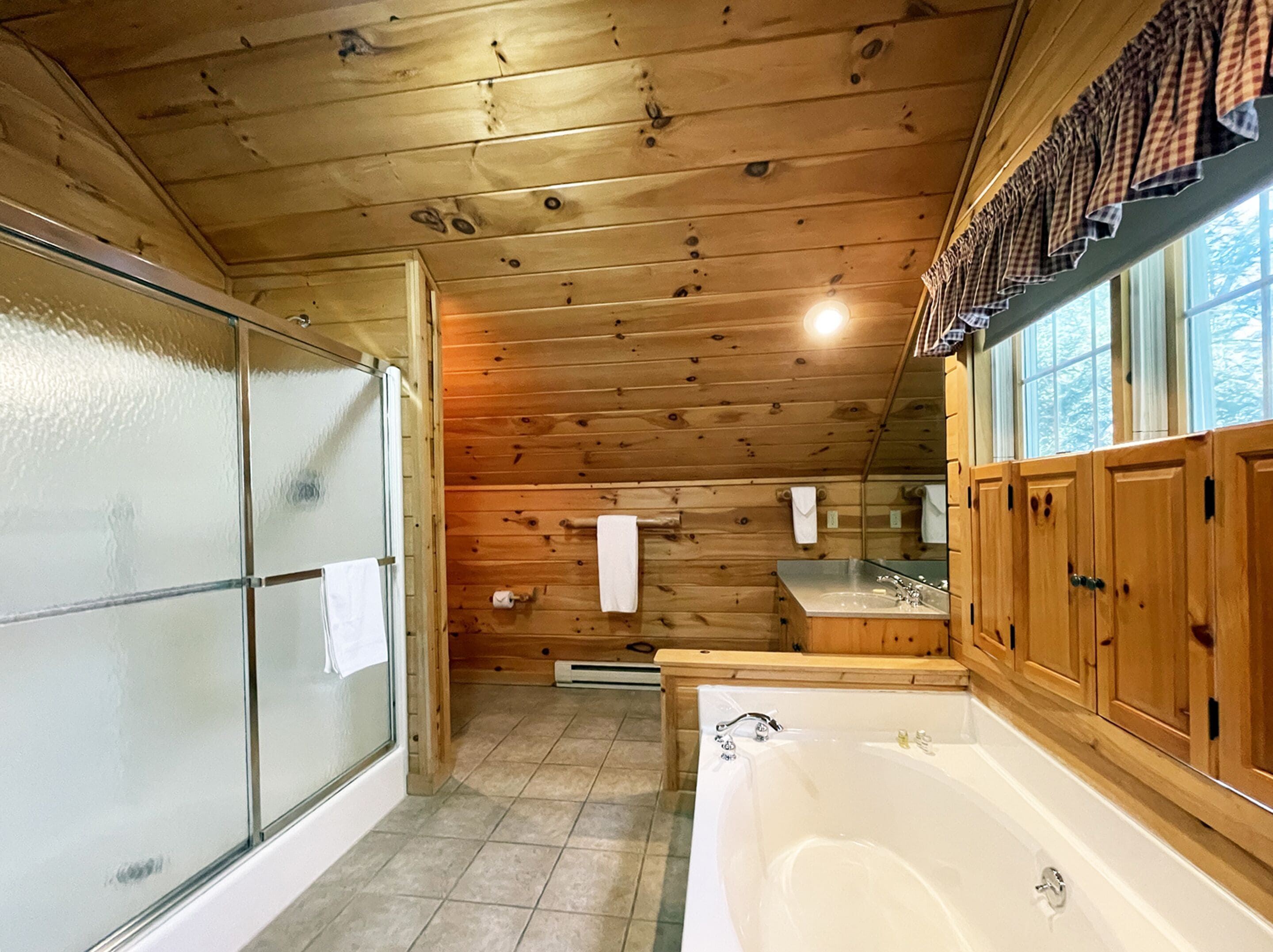 A wooden cabin bathroom with a glass shower, a bathtub, and wooden cabinets.