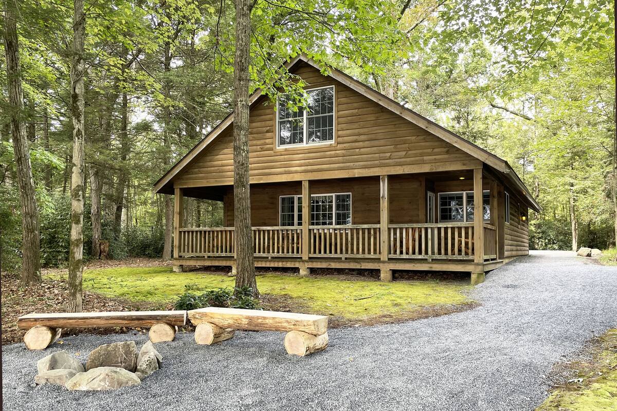 A wooden cabin with a porch, surrounded by trees.
