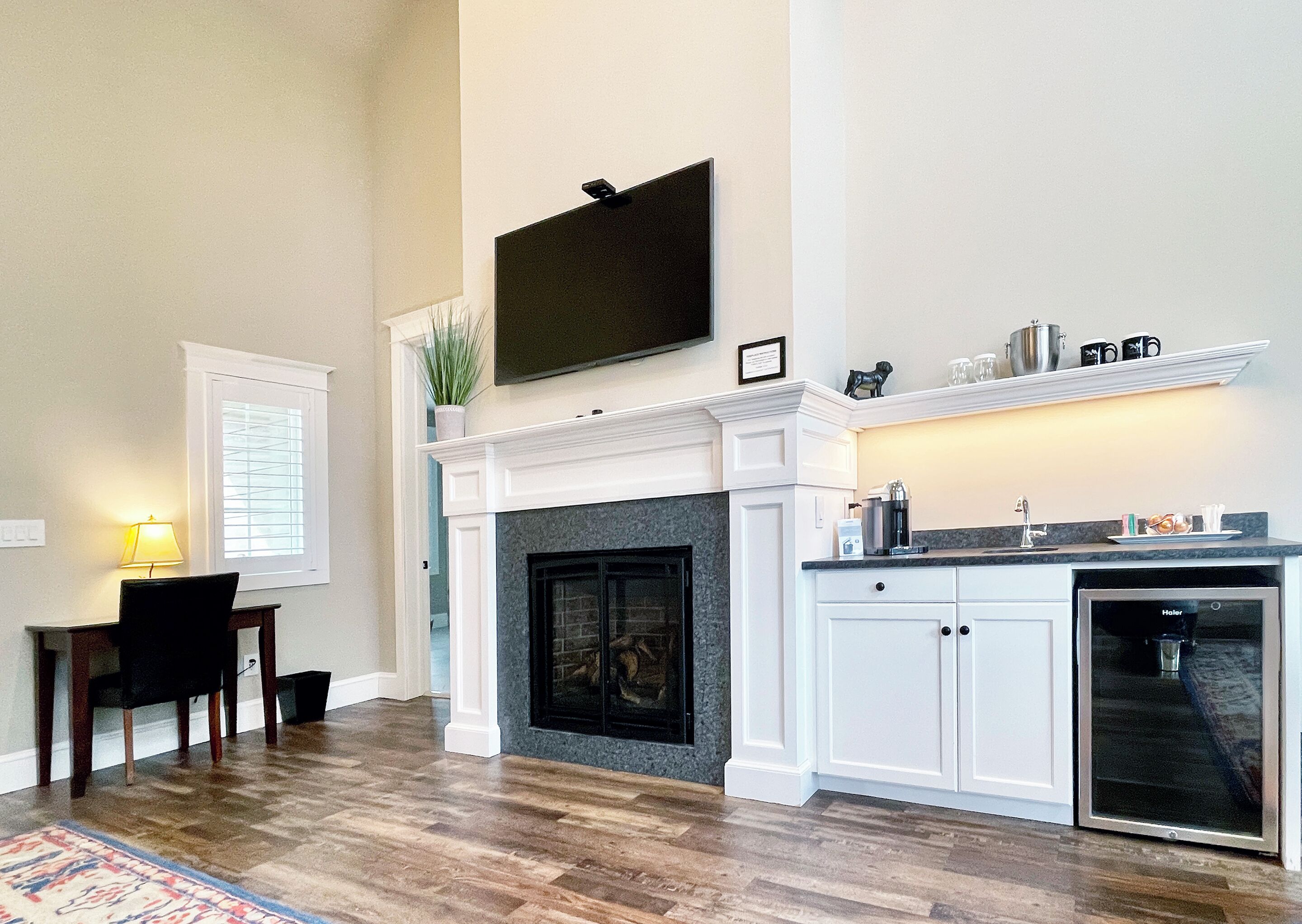 A spacious living room with a fireplace, a dining area with a table and chairs, and a kitchen area with a dishwasher and a coffee maker.
