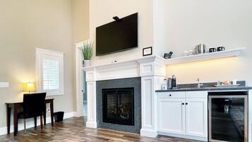 A spacious living room with a fireplace, a dining area with a table and chairs, and a kitchen area with a dishwasher and a coffee maker.