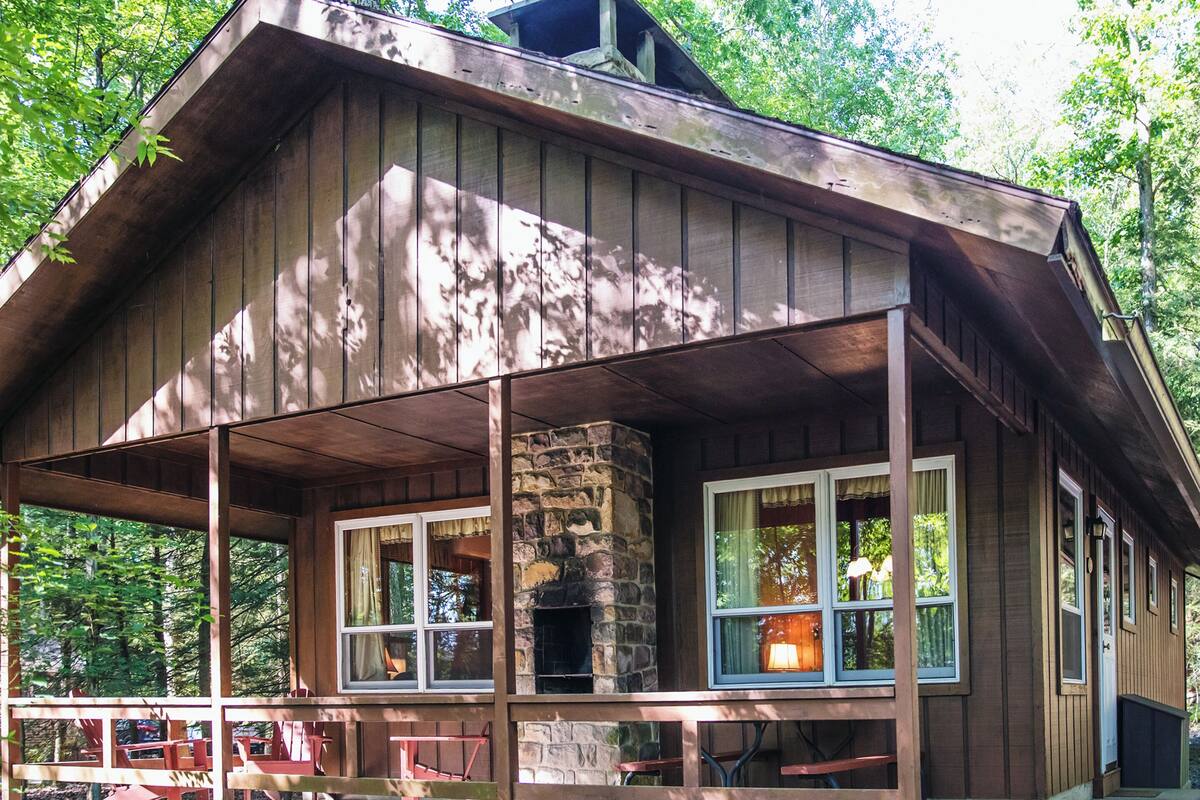 A rustic cabin with a stone fireplace, wooden porch, and picnic tables.