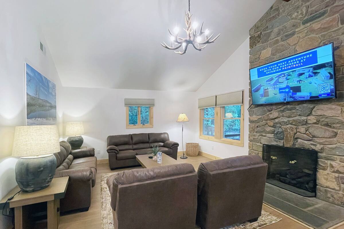 A living room with a stone fireplace, a large flat-screen TV mounted on the wall, and a comfortable seating area with a sofa and armchairs.