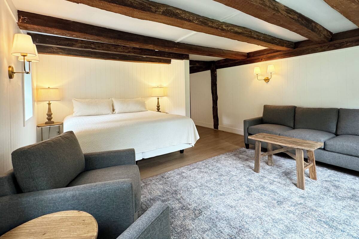 A bedroom with a large bed, two bedside lamps, a grey sofa, a small wooden table, and a grey rug.