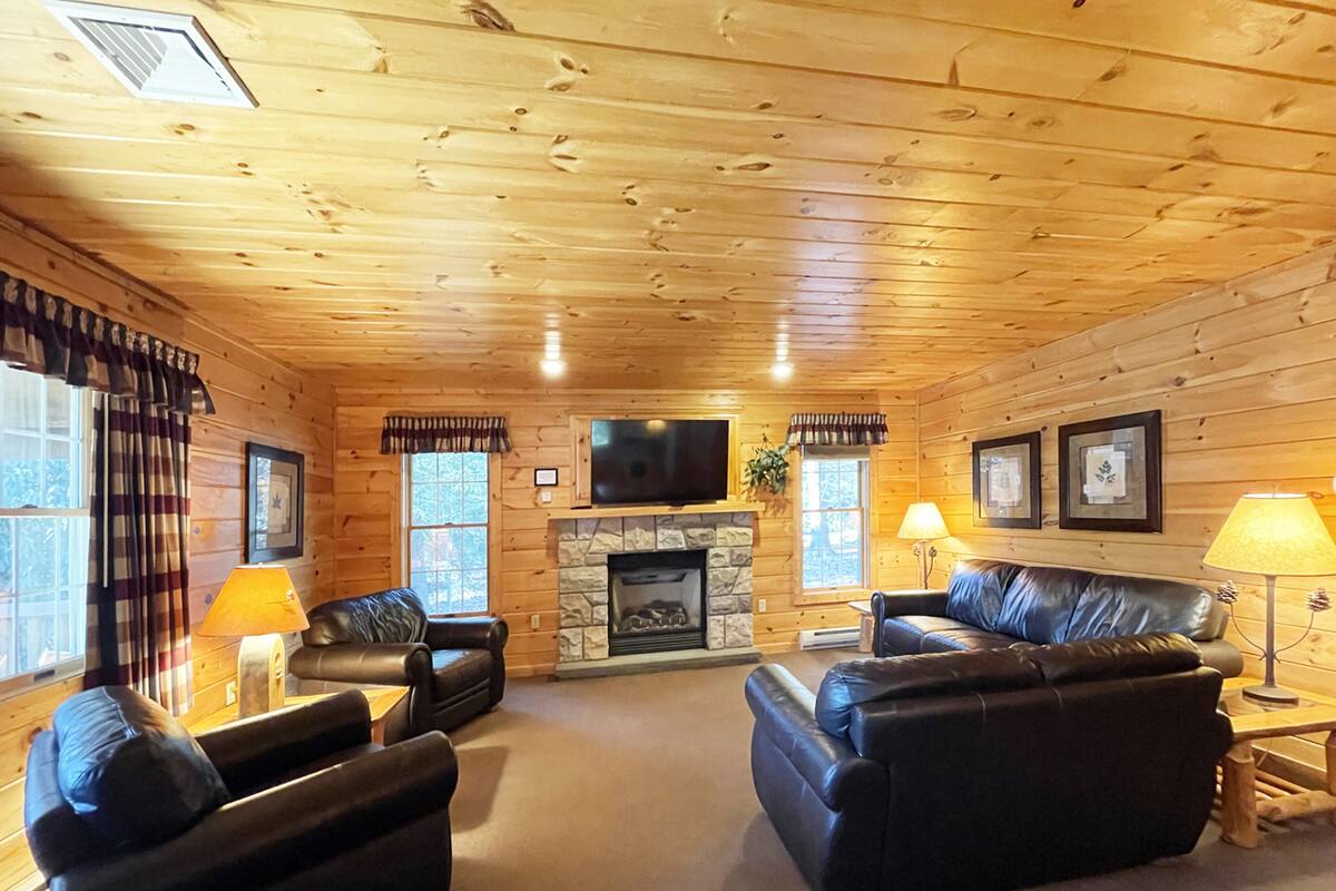 A log cabin interior with a fireplace, leather sofas, and a television.